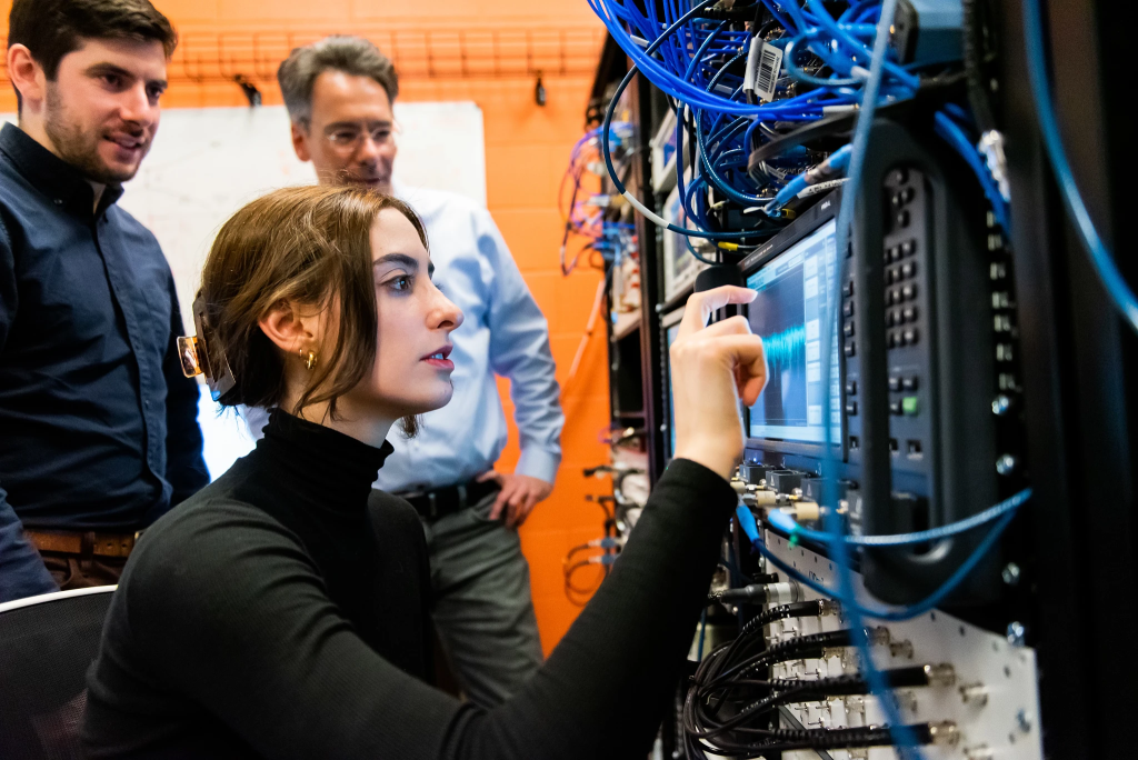 A QIS scientist adjusts electronics while two other researchers look on.