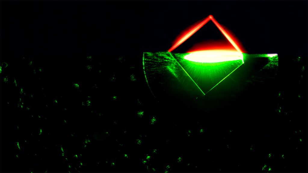 A green laser shines on a diamond, causing red fluorescence.